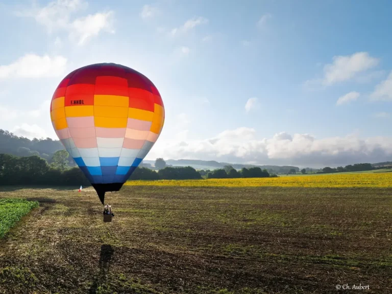 Montgolfière colorée de L'Air du Perche flottant au-dessus d'un champ au lever du soleil.