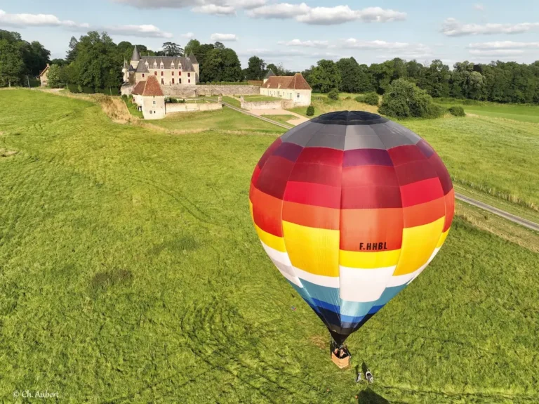 Vue aérienne de la montgolfière de L'Air du Perche volant près d'un château dans un paysage verdoyant.