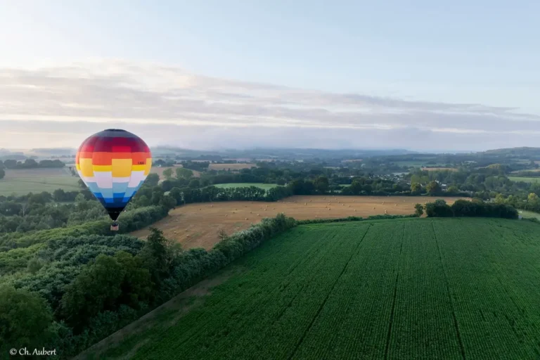 Montgolfière de L'Air du Perche dans le ciel au lever du soleil, avec une brume légère couvrant les champs.