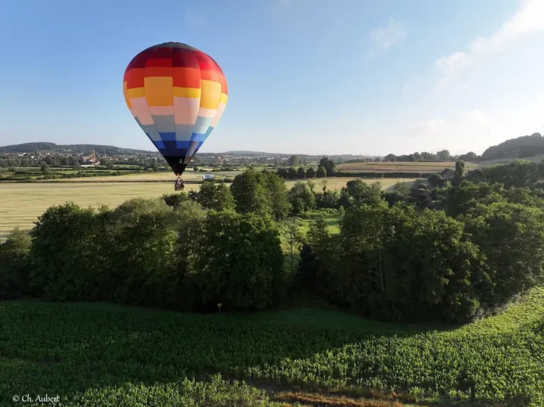 Montgolfière de L'Air du Perche survolant un paysage rural avec des champs et des arbres.