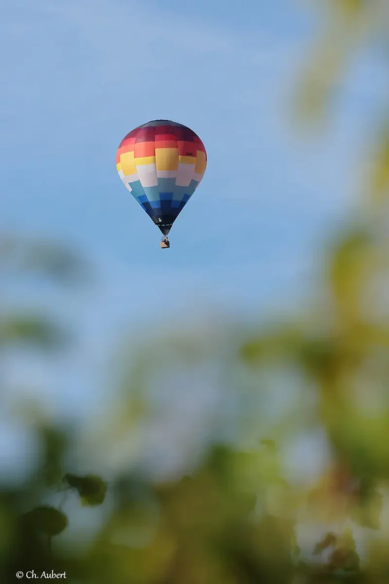 Montgolfière de L'Air du Perche en pleine ascension, capturée depuis une perspective lointaine.